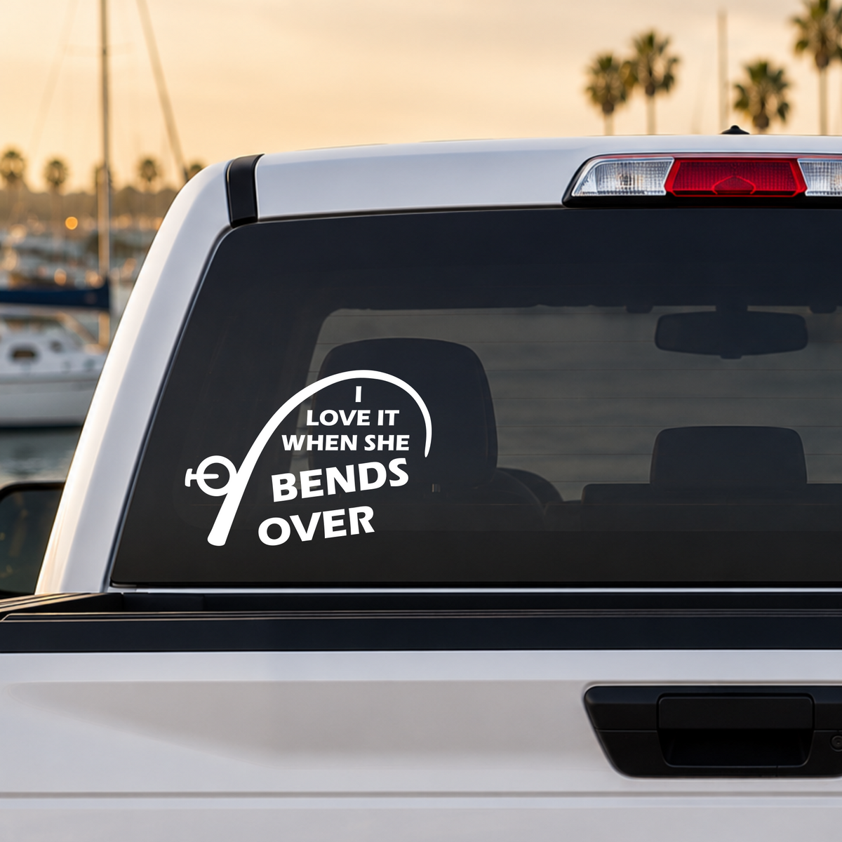 White I Love It When She Bends Over fishing rod vinyl decal applied to a truck rear window featuring original KD artwork. Made in the USA.
